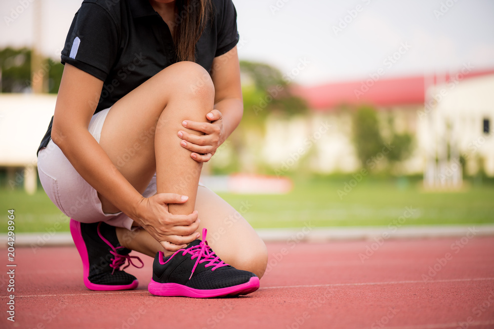 Naklejka premium Ankle sprained. Young woman suffering from an ankle injury while exercising and running on Running Track. Healthcare and sport concept.