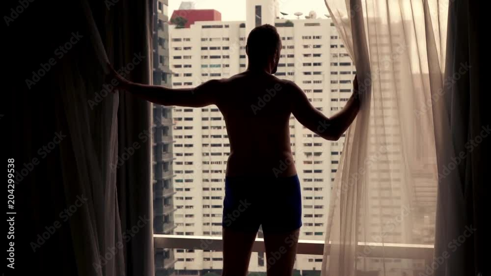 Young man unveil curtains and admire city view from the window.
Young man unveil curtains and admire city view from the window.