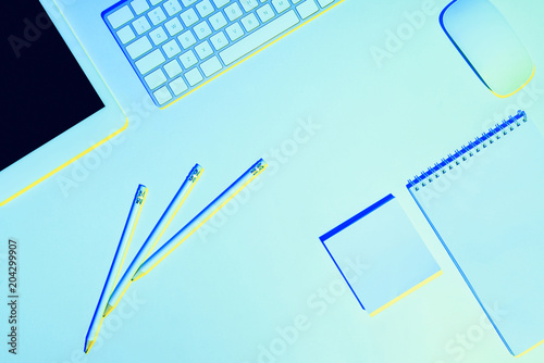 blue toned picture of pencils, digital tablet, computer keyboard and mouse, textbook and sticky note