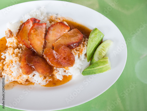 Red pork with rice, topped with red water in the dish, white on green table.