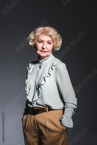 beautiful senior woman in stylish shirt looking at camera on dark grey