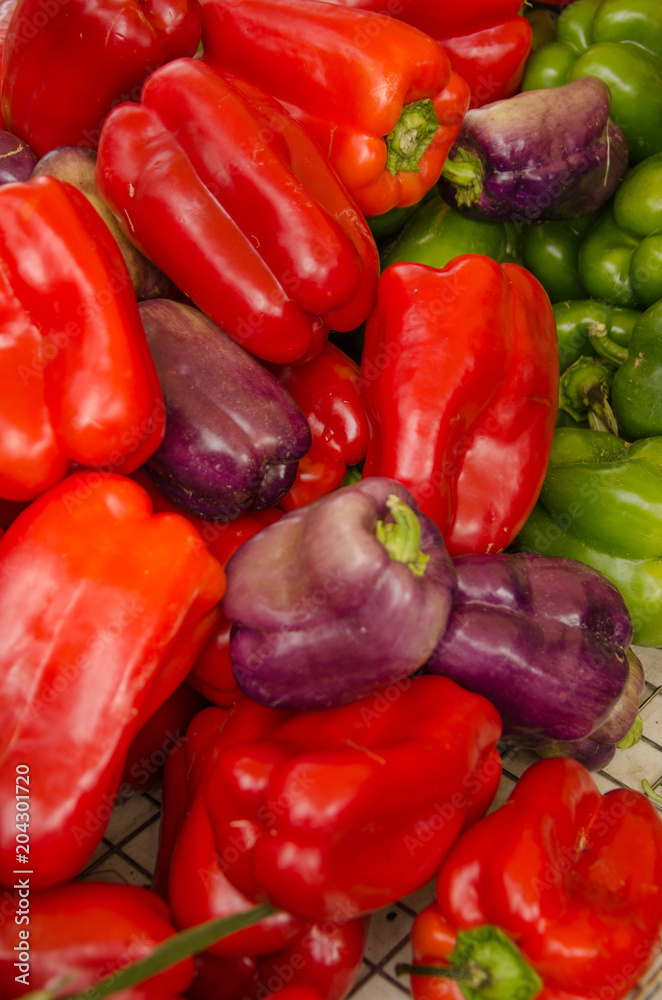 Several red, green, and purple bell peppers at farm stand Several red, green, and purple bell peppers at farm stand