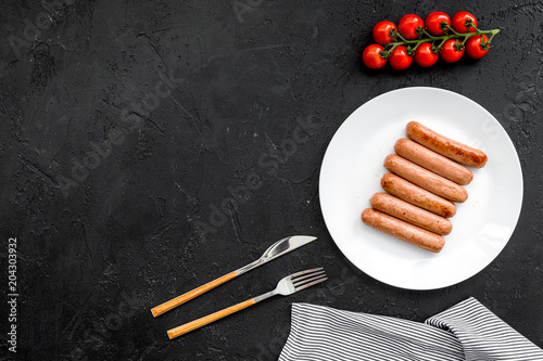 Dish on the grill fast and easy to cook. Fried sausages near cherry tomatoes on black background top view copy space