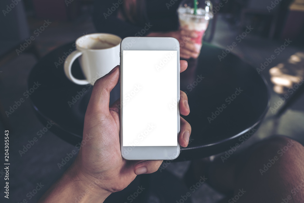 Mockup image of hand holding white mobile phone with blank screen in cafe and blur woman in background