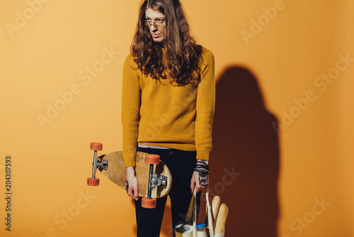 handsome skater holding longboard and bag with food, on yellow