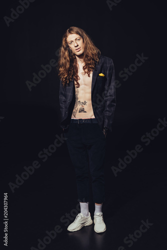 young elegant man with long hair and tattoos, on black