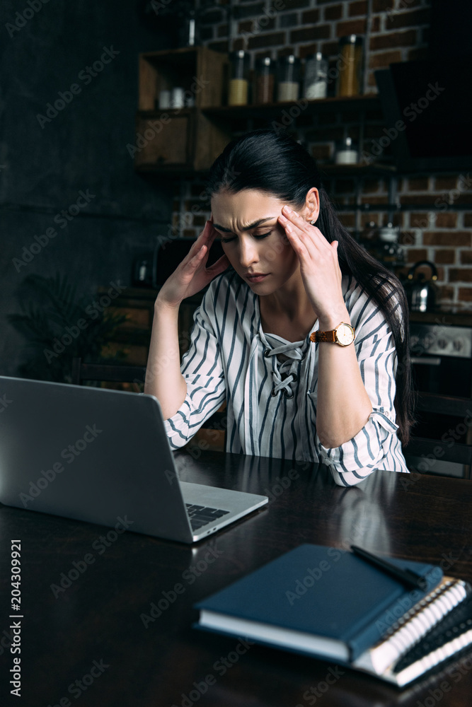 stressed young woman with headache sitting on kitchen with laptop - obrazy, fototapety, plakaty 