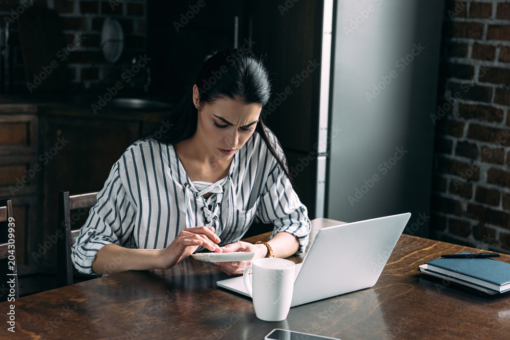 young woman with calculator and laptop counting tax at home on kitchen young woman with calculator and laptop counting tax at home on kitchen
