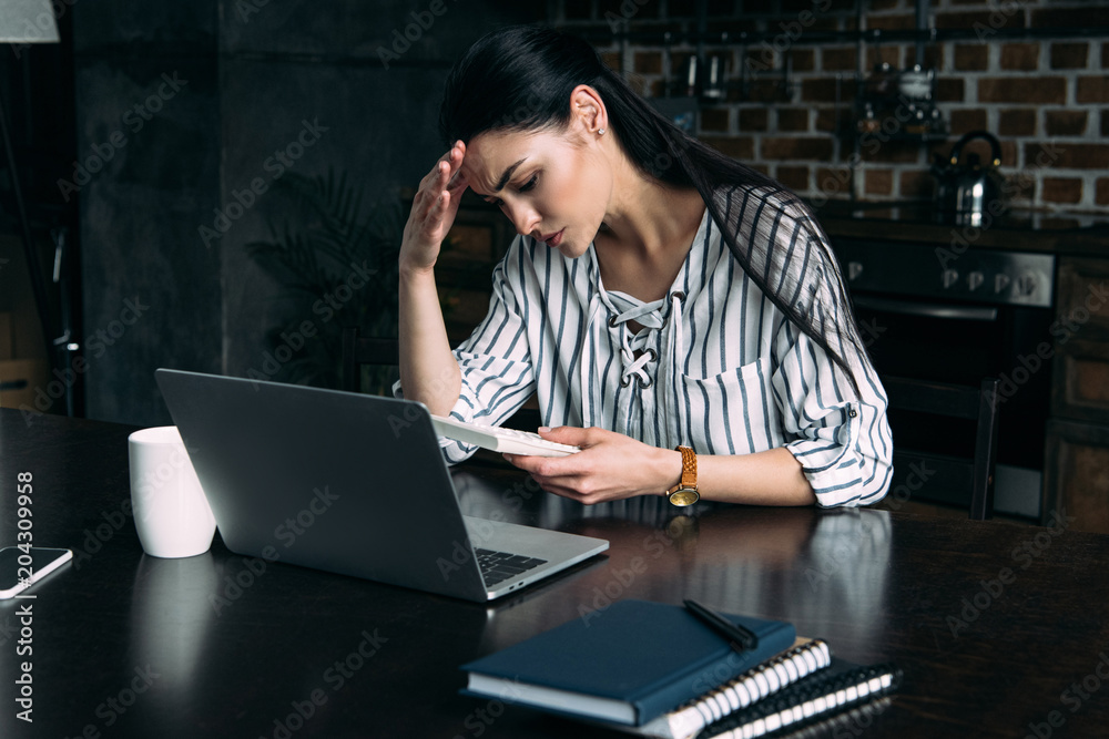 depressed young woman with calculator and laptop counting tax at home on kitchen depressed young woman with calculator and laptop counting tax at home on kitchen