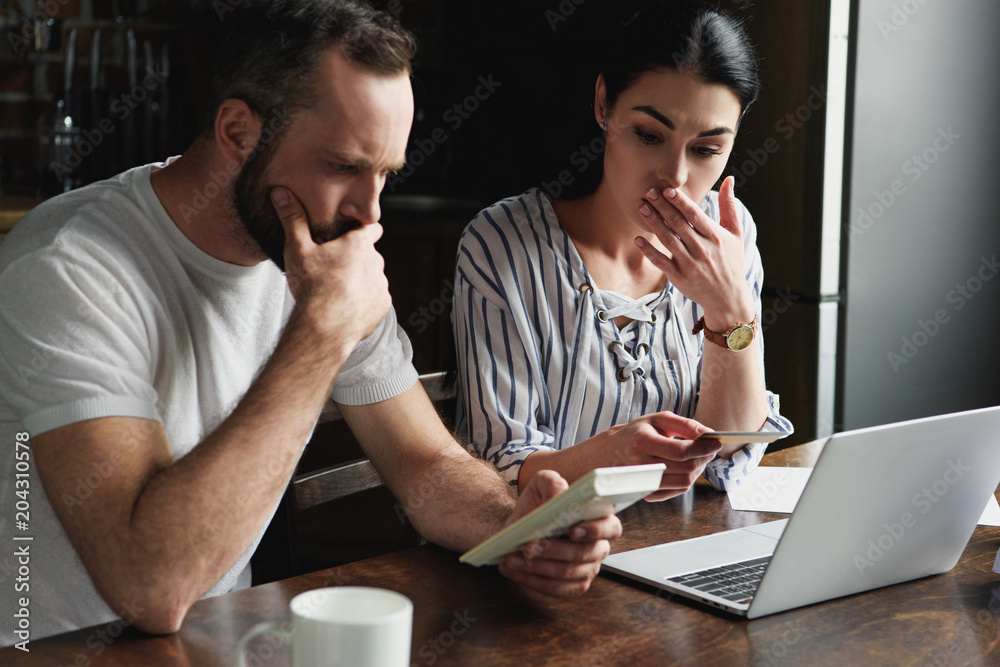 depressed young couple counting tax and bills with laptop and calculator depressed young couple counting tax and bills with laptop and calculator