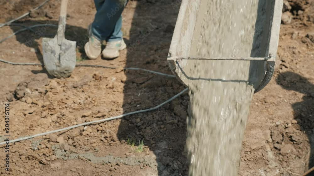Work on the construction of a suburban house. From the mixer concrete flows, next to a worker with a shovel Work on the construction of a suburban house. From the mixer concrete flows, next to a worker with a shovel