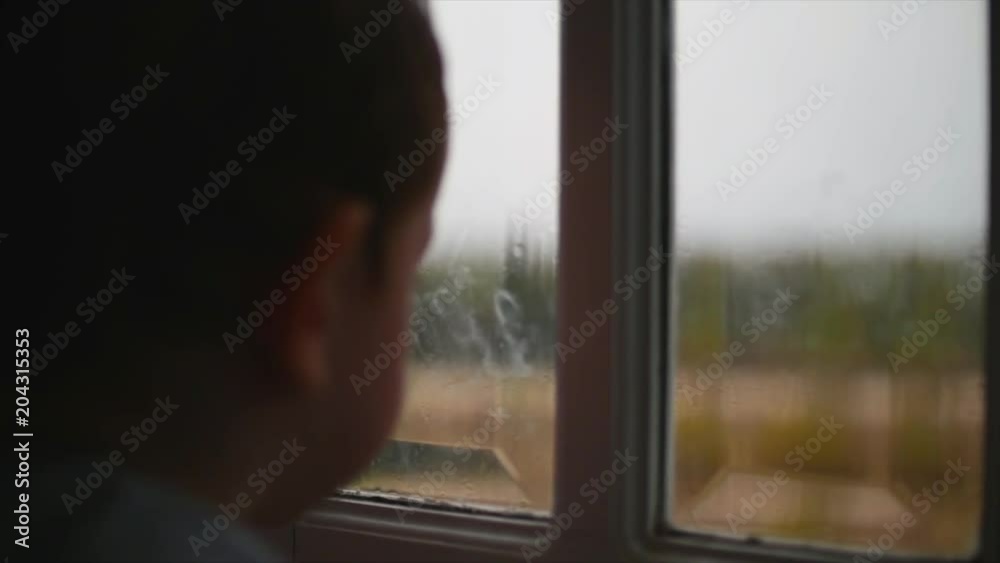 Child looks at the rain behind the window. Stock Footage.