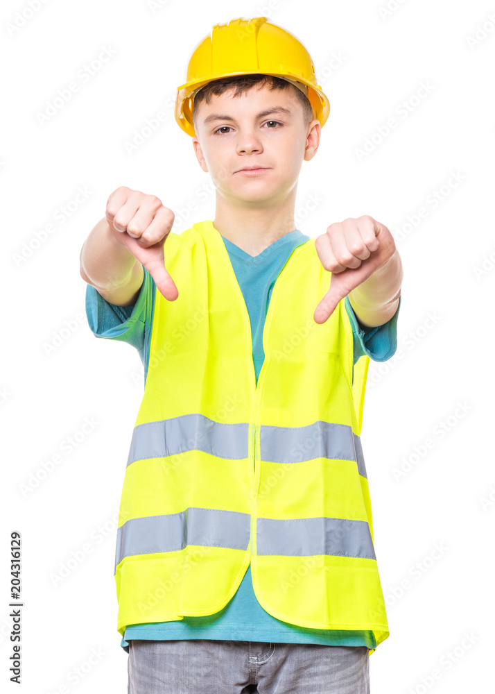 Emotional portrait of handsome child wearing safety jacket and yellow hard hat. Unhappy teen boy giving thumbs down hand gesture and looking at camera, isolated on white background. Emotional portrait of handsome child wearing safety jacket and yellow hard hat. Unhappy teen boy giving thumbs down hand gesture and looking at camera, isolated on white background.
