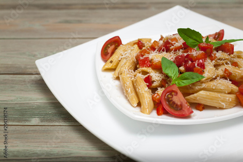 Penne pasta with vegetables and parmesan cheese on a white square plate on a wooden table.