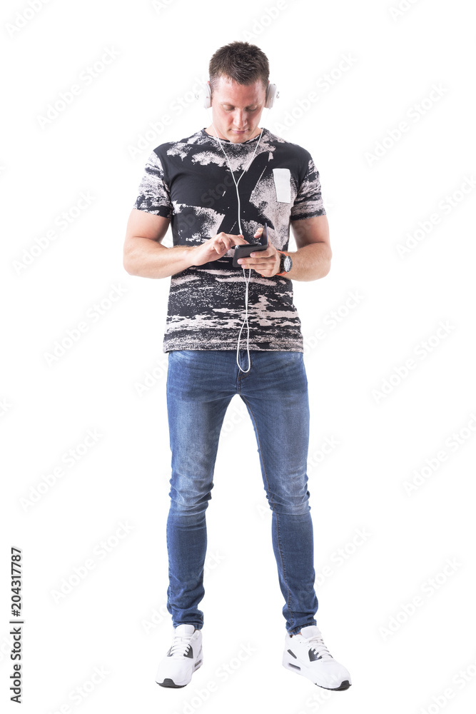 Front view of young adult man with headphones on head browsing music on smartphone device. Full body isolated on white background. Front view of young adult man with headphones on head browsing music on smartphone device. Full body isolated on white background.