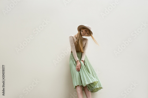 Young red hair girl in hat, dressed in beige blouse and turqoise pleats skirt, on light street backgraund.  Fashion and stylish concept.