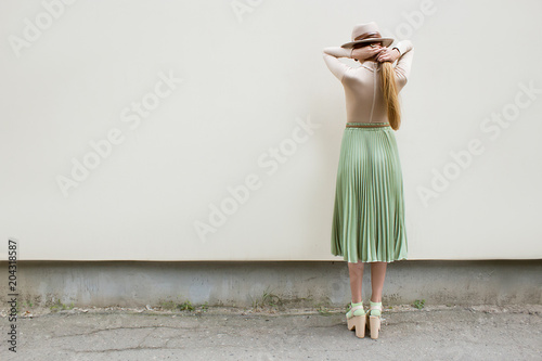 Young red hair girl in hat, dressed in beige blouse and turqoise pleats skirt, on light street backgraund.  Fashion and stylish concept.