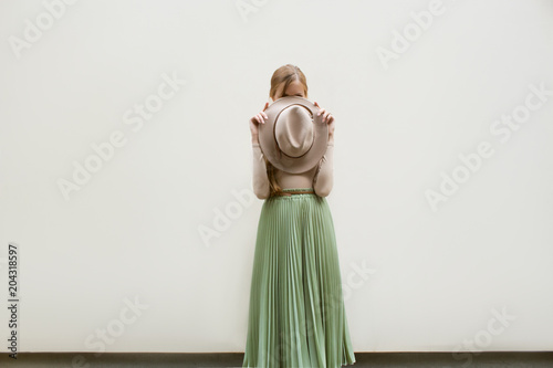 Young red hair girl in hat, dressed in beige blouse and turqoise pleats skirt, on light street backgraund.  Fashion and stylish concept.
