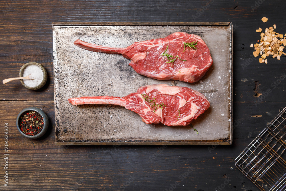 Raw Tomahawk steak on on old metal tray ondark old wooden background with spices for grilling or preparation for smoking, top view, copy space