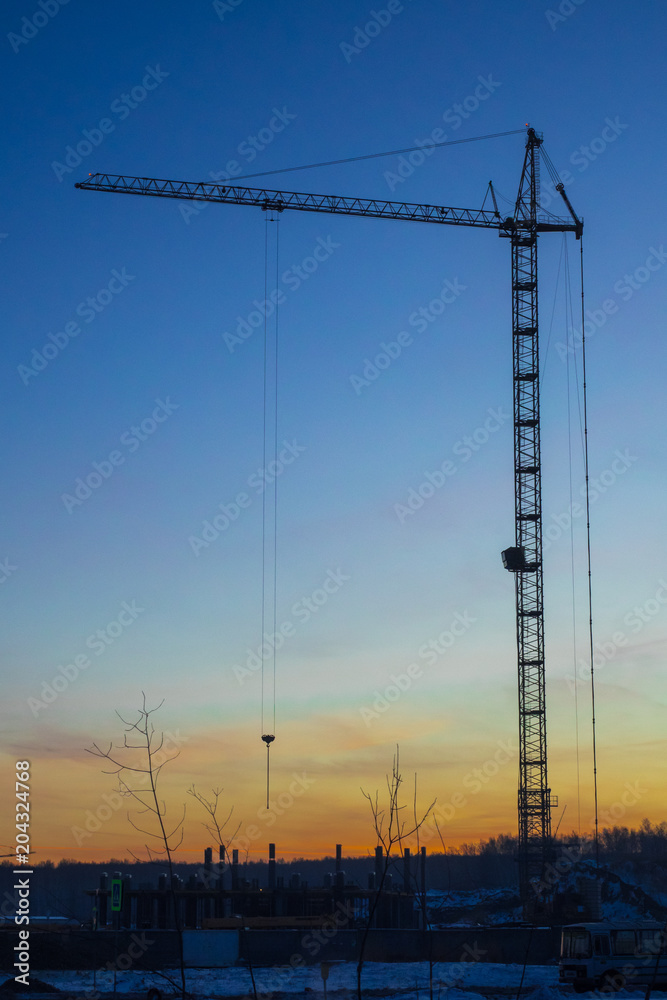 High-rise building, crane, blue sky, white clouds in the light of the setting sun