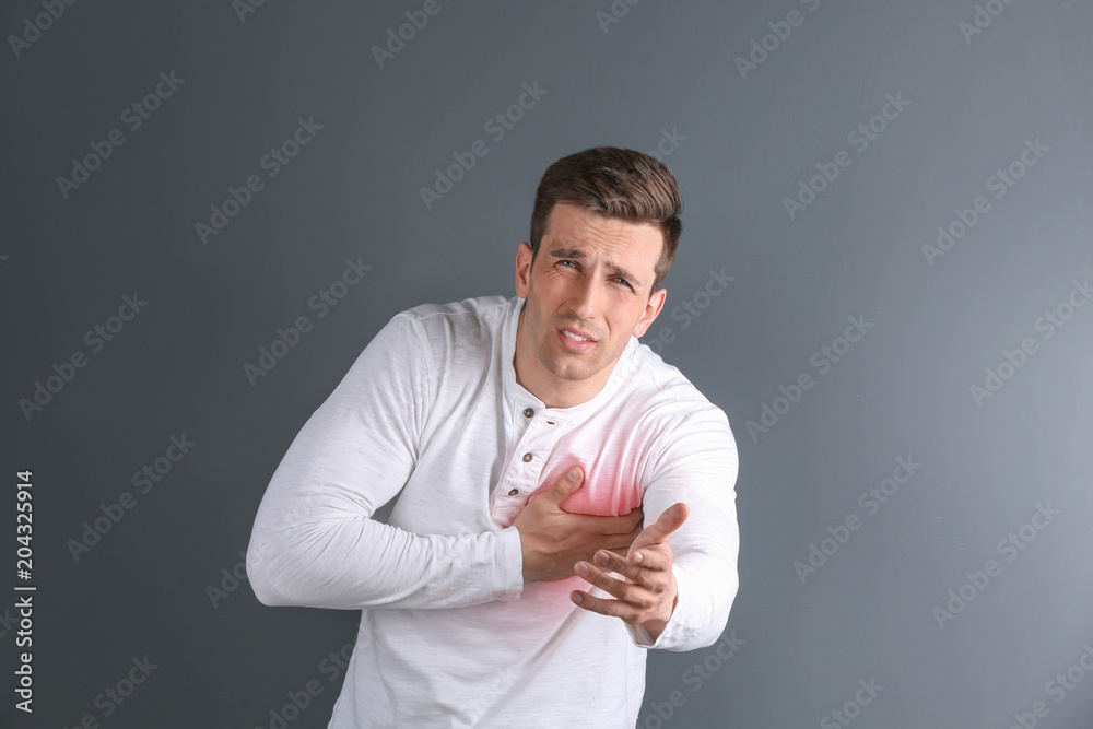 Young man having heart attack on gray background Young man having heart attack on gray background