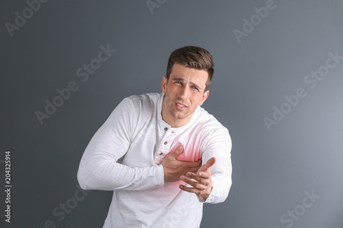 Young man having heart attack on gray background © New Africa
