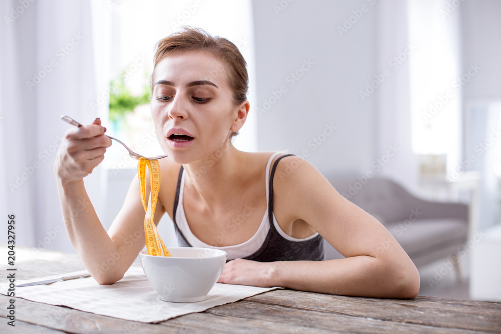 Health problem. Pleasant young woman trying to eat while suffering from anorexia