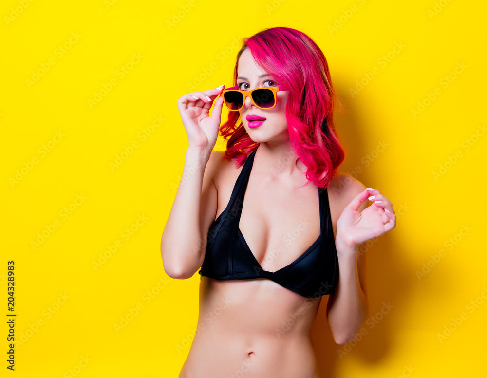 Young pink hair girl in bikini and orange glasses. Portrait isolated on yellow background