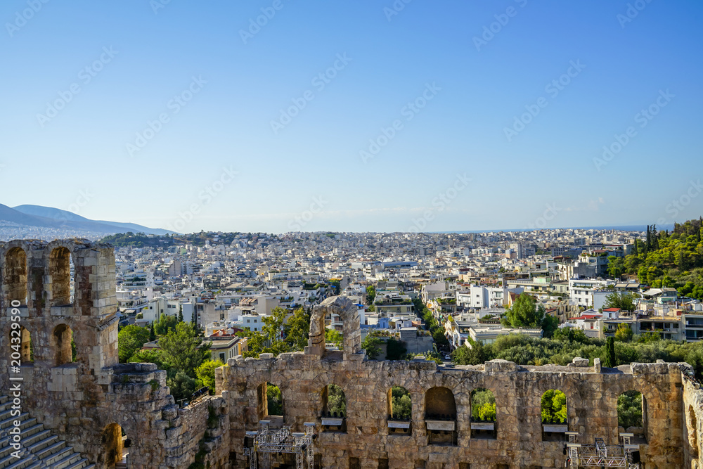 View of Athens cityscape through ancient stone theatre seeing lowrise white buildings architecture, mountain, trees and clear blue sky background
