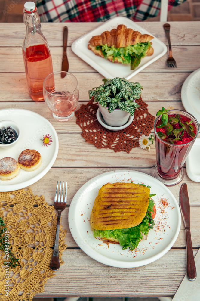 breakfast served cafe table with cheese pancakes, sandwich, croissant and drinks. Top view