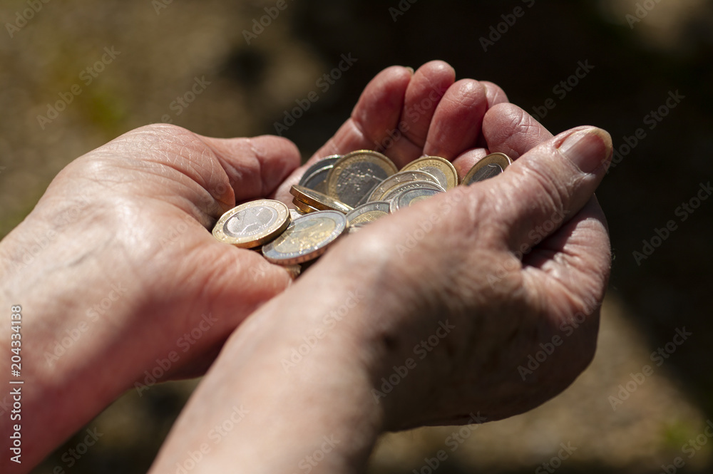 Two hands of an old woman hold out many euro coins. O