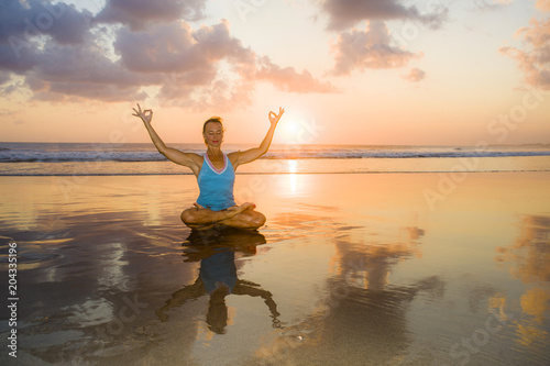 young fit and attractive sport woman in beach sunset yoga practice workout sitting on wet sun in front of the sea in meditation and relaxation exercise