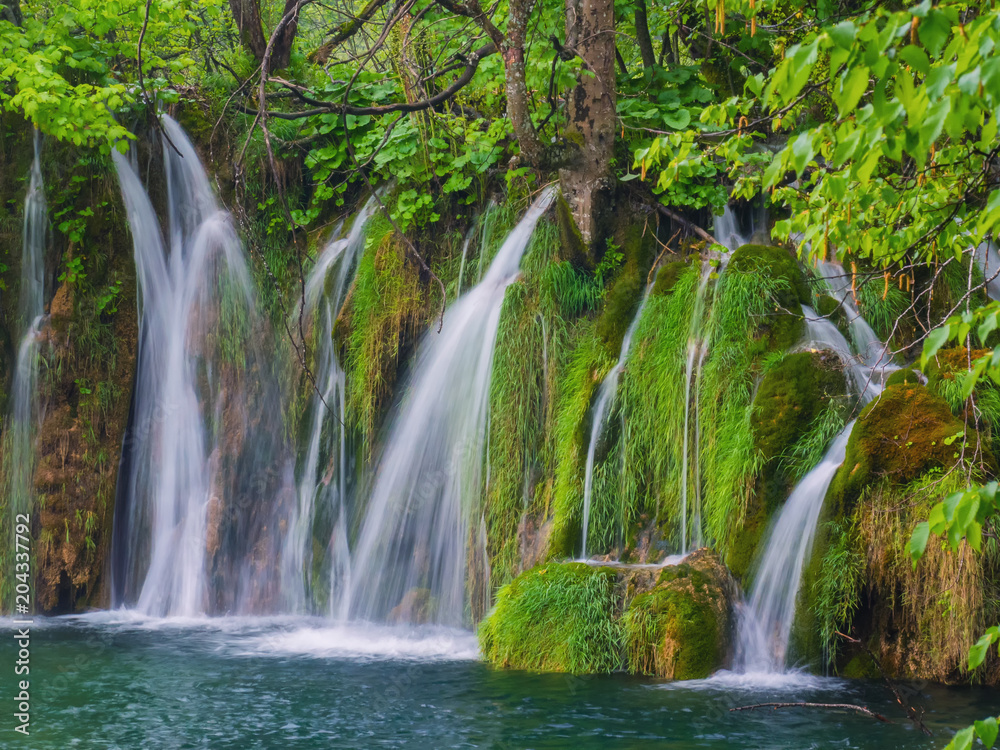 Fototapeta premium Scenic waterfall deep in the forest with streams of crystal clear water and moss on the stones.