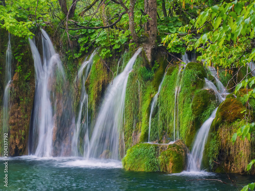 Scenic waterfall deep in the forest with streams of crystal clear water and moss on the stones.