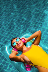 amazing beautiful girl in a yellow bikini air mattress swims in the pool of a luxury hotel, summer vacation, happiness, travel, smile joy, listening to music, drinking cocktail
