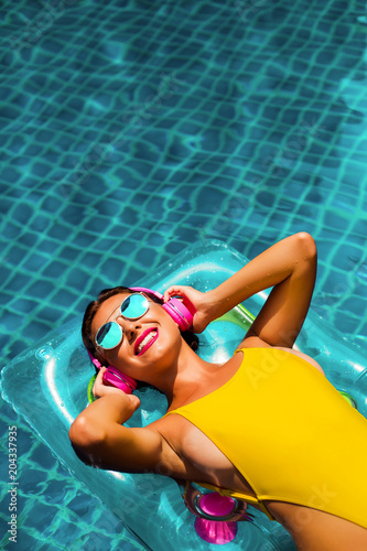 amazing beautiful girl in a yellow bikini air mattress swims in the pool of a luxury hotel, summer vacation, happiness, travel, smile joy, listening to music, drinking cocktail