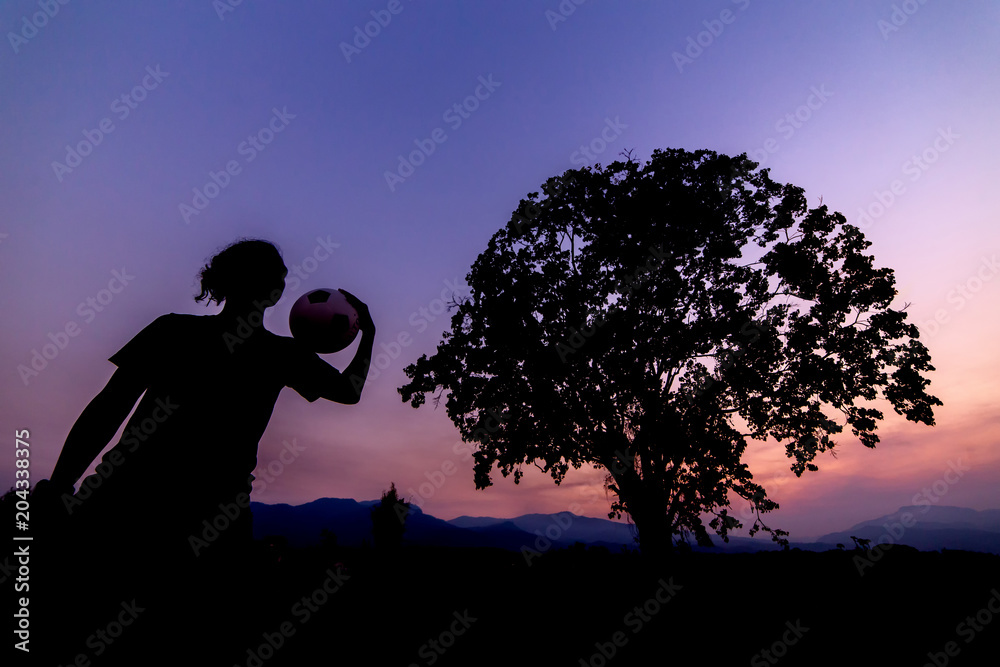 Young man is practicing Football under a big tree in the sunset. Silhouette style.