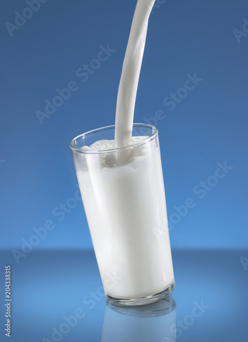 Pouring Milk Splash in A Glass Over Blue Background
