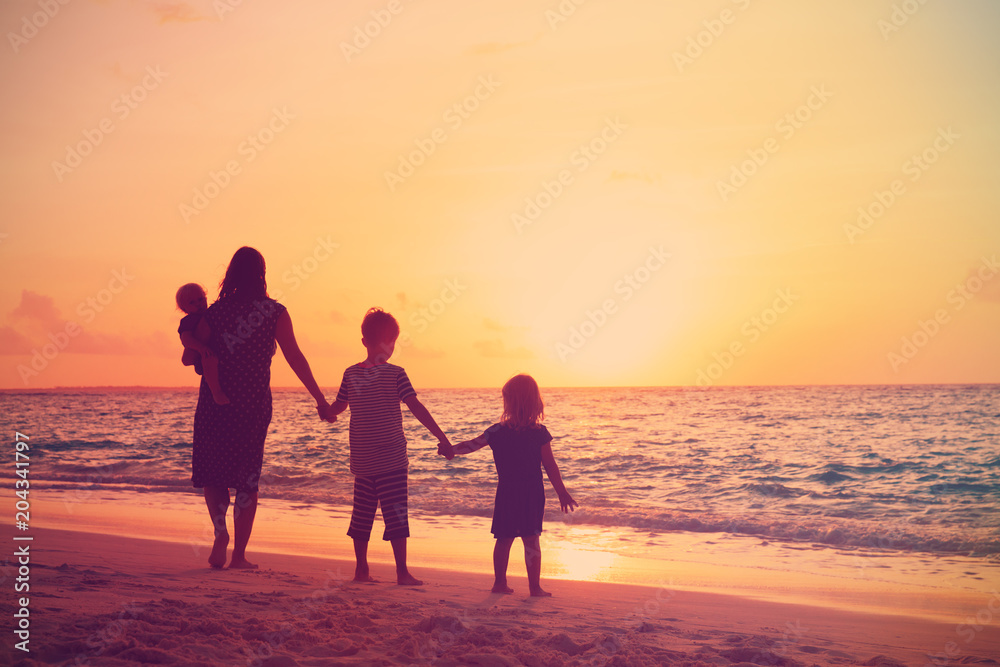 mother with kids walking on beach at sunset