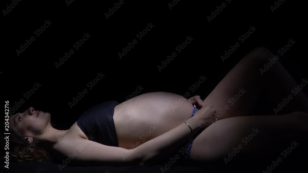 Pregnant woman lies in the dark and looks up, camera zoom