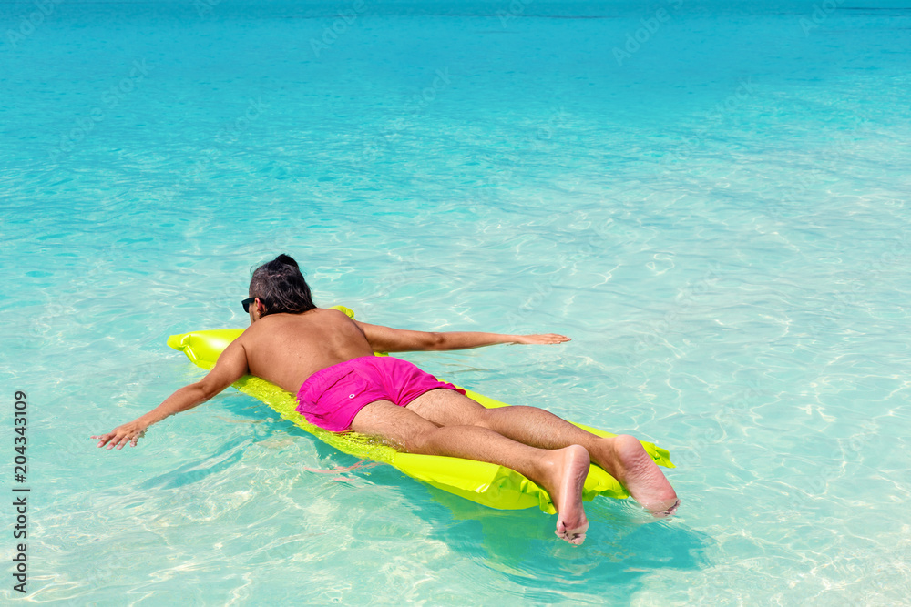 Man with inflatable green mattress on beach