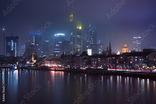 Picturesque view of business district with skyscrapers and Old Town with mirror reflections in the river during foggy morning blue hour  Frankfurt am Main  Germany