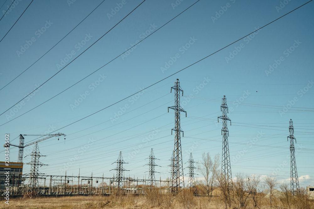Group of posts with wires of high voltage on background of blue sky. Background image of pillars and wires in sky with copy space. Building on backdrop.