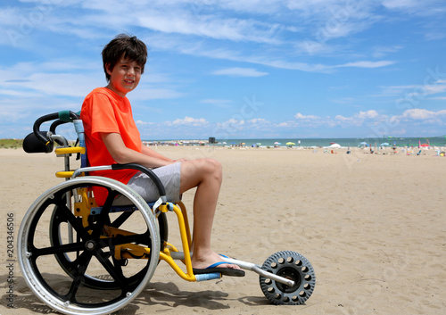boy with disabilities on wheelchair in the beach near the sea in