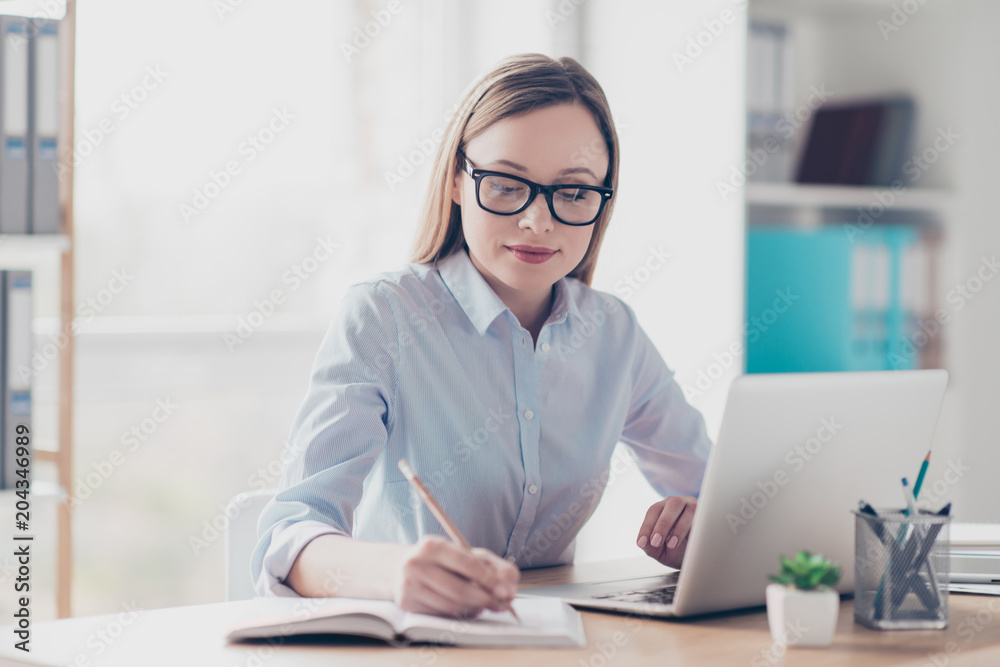 Portrait of charming director, pretty, nice woman holding pencil in hand, writing a date of conversation in reminder, organizing her day, sitting in work place, station at desktop Portrait of charming director, pretty, nice woman holding pencil in hand, writing a date of conversation in reminder, organizing her day, sitting in work place, station at desktop