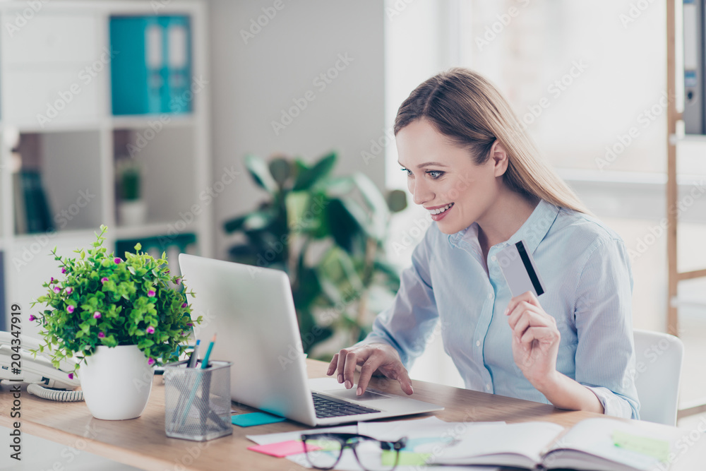 Portrait of attractive, cheerful, positive woman holding credit card in hand, making shopping through internet so easy and comfortable during work time sitting in work place, station Portrait of attractive, cheerful, positive woman holding credit card in hand, making shopping through internet so easy and comfortable during work time sitting in work place, station