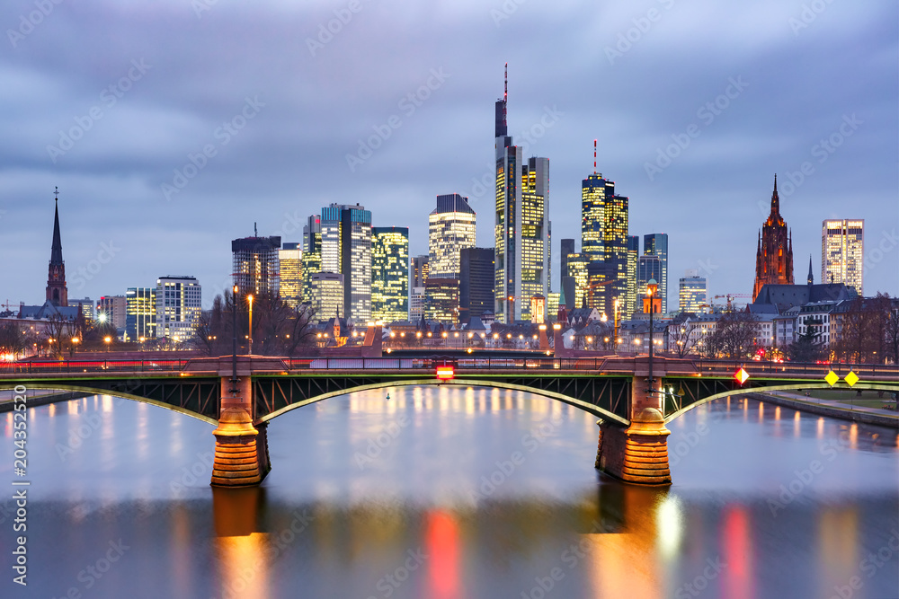 Picturesque view of Frankfurt am Main skyline and Ignatz Bubis Brucke bridge during evening blue hour with mirror reflections in the river, Germany