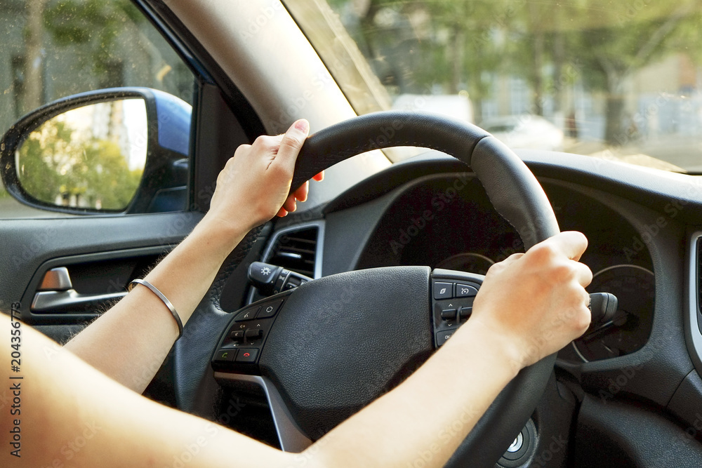 Close up of young woman hands holding steering wheel while driving car. Dashboard panel, phone holder mount, windshield. Businesswoman man inside vehicle interior in a daylight. Background, side view. Close up of young woman hands holding steering wheel while driving car. Dashboard panel, phone holder mount, windshield. Businesswoman man inside vehicle interior in a daylight. Background, side view.