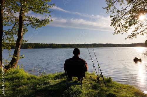 Fisherman sitting on the chair and fishing on the shore of lake