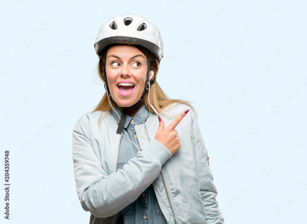 Young woman with bike helmet and earphones pointing away side with finger Young woman with bike helmet and earphones pointing away side with finger